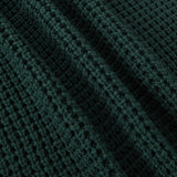 Close-up of a dark forest green waffle-knit fabric texture with soft folds.
