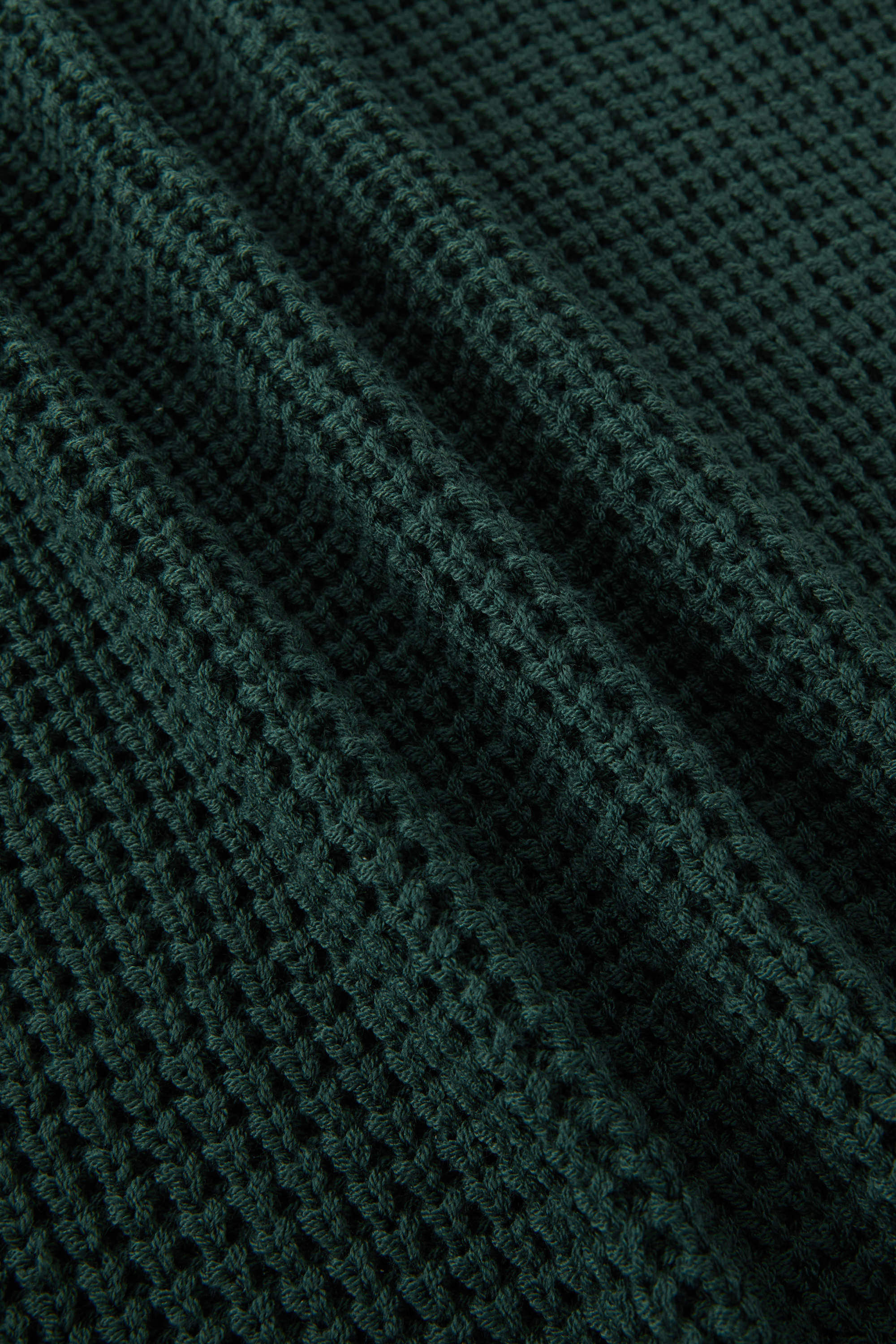 Close-up of a dark forest green waffle-knit fabric texture with soft folds.