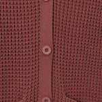 Close-up of a waffle-knit cardigan in a dusty rose or mauve color, featuring a matching button placket and ribbed collar.