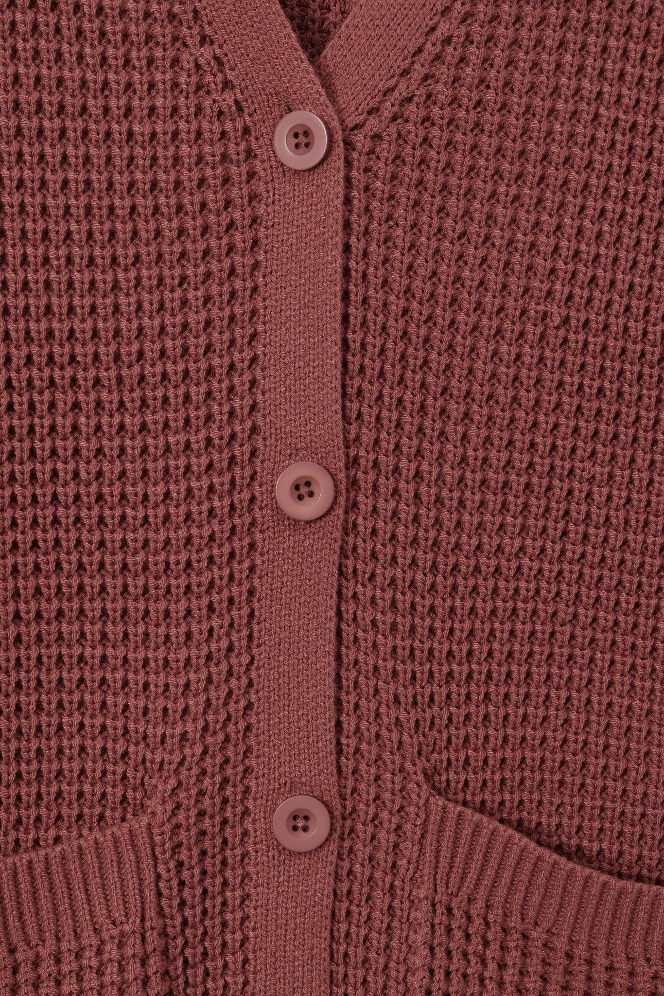 Close-up of a waffle-knit cardigan in a dusty rose or mauve color, featuring a matching button placket and ribbed collar.