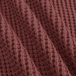 Close-up of a textured knit fabric in a muted dusty rose or mauve-brown color, showing the detailed ribbed pattern and soft folds.