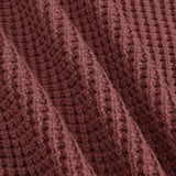Close-up of a textured knit fabric in a muted dusty rose or mauve-brown color, showing the detailed ribbed pattern and soft folds.