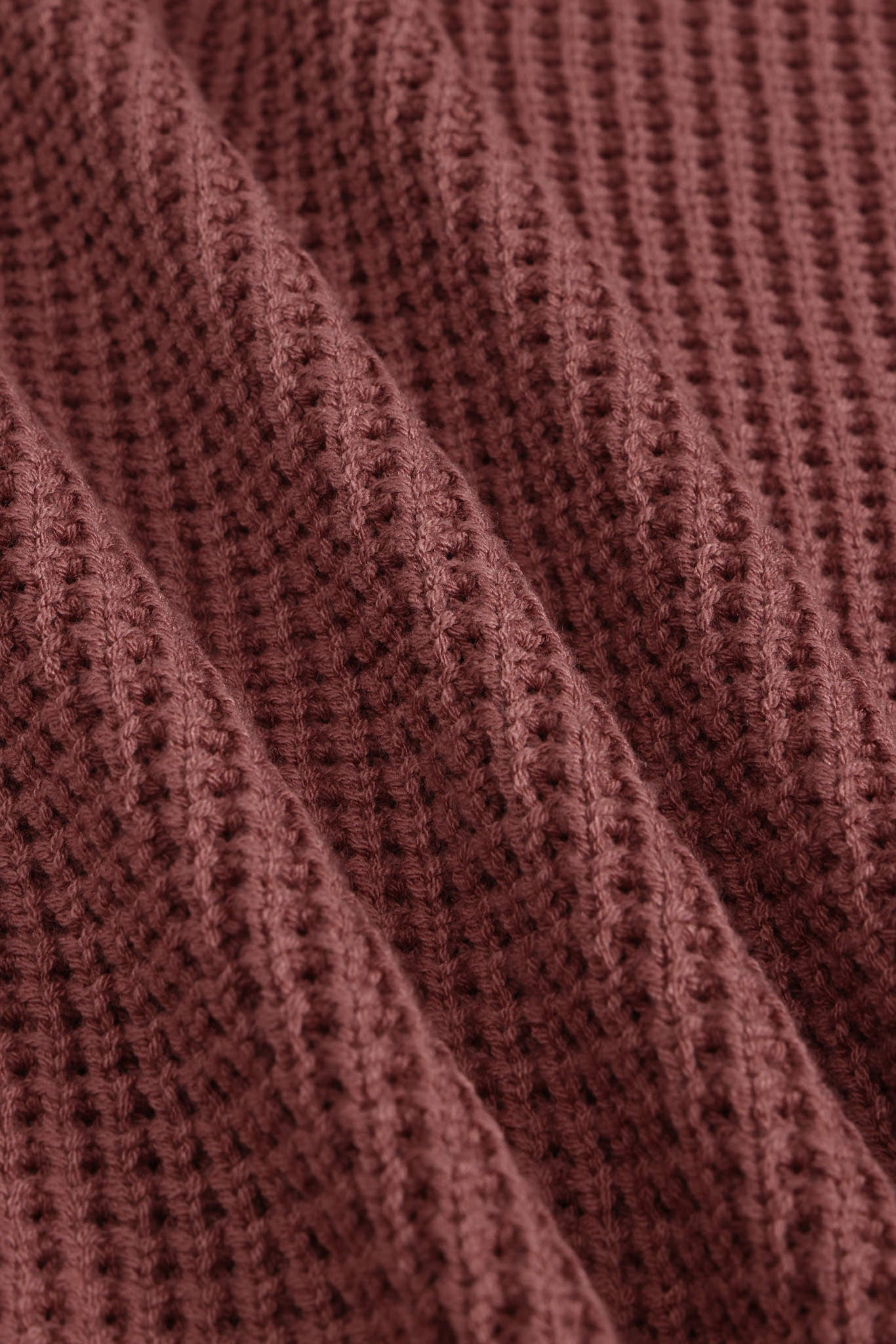 Close-up of a textured knit fabric in a muted dusty rose or mauve-brown color, showing the detailed ribbed pattern and soft folds.