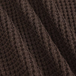 Close-up of a dark brown waffle-knit fabric with soft diagonal folds showing the textured knit pattern.