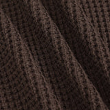 Close-up of a dark brown waffle-knit fabric with soft diagonal folds showing the textured knit pattern.