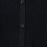 Close-up of a black waffle-knit cardigan sweater showing the button closure and ribbed collar.