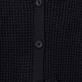 Close-up of a black waffle-knit cardigan sweater showing the button closure and ribbed collar.