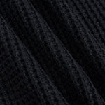 Close-up of a black ribbed knit fabric with a waffle or textured weave, shown in soft diagonal folds.