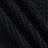 Close-up of a black ribbed knit fabric with a waffle or textured weave, shown in soft diagonal folds.