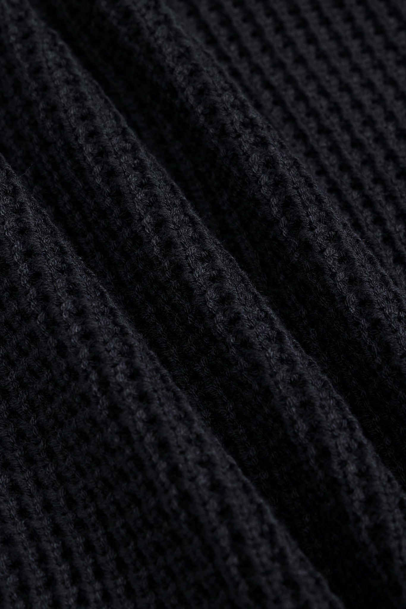 Close-up of a black ribbed knit fabric with a waffle or textured weave, shown in soft diagonal folds.