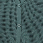 Close-up of a textured knit cardigan in a muted sage green color, featuring a V-neckline, three front buttons, and ribbed trim.