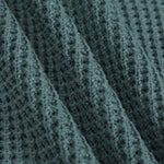 Close-up of a textured knit fabric with a waffle or basketweave pattern in a muted blue-gray color, shown with soft folds.