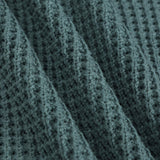 Close-up of a textured knit fabric with a waffle or basketweave pattern in a muted blue-gray color, shown with soft folds.