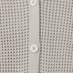 Close-up of a textured knit cardigan in a light warm gray or oatmeal tone, featuring a button placket with white buttons.