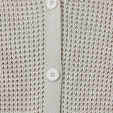 Close-up of a textured knit cardigan in a light warm gray or oatmeal tone, featuring a button placket with white buttons.