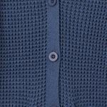 Close-up of a textured knit cardigan in a muted slate blue color, featuring a buttoned front closure and ribbed trim.