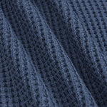 Close-up of a textured navy blue knit fabric with a waffle or open-stitch pattern, shown with soft folds.