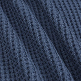 Close-up of a textured navy blue knit fabric with a waffle or open-stitch pattern, shown with soft folds.