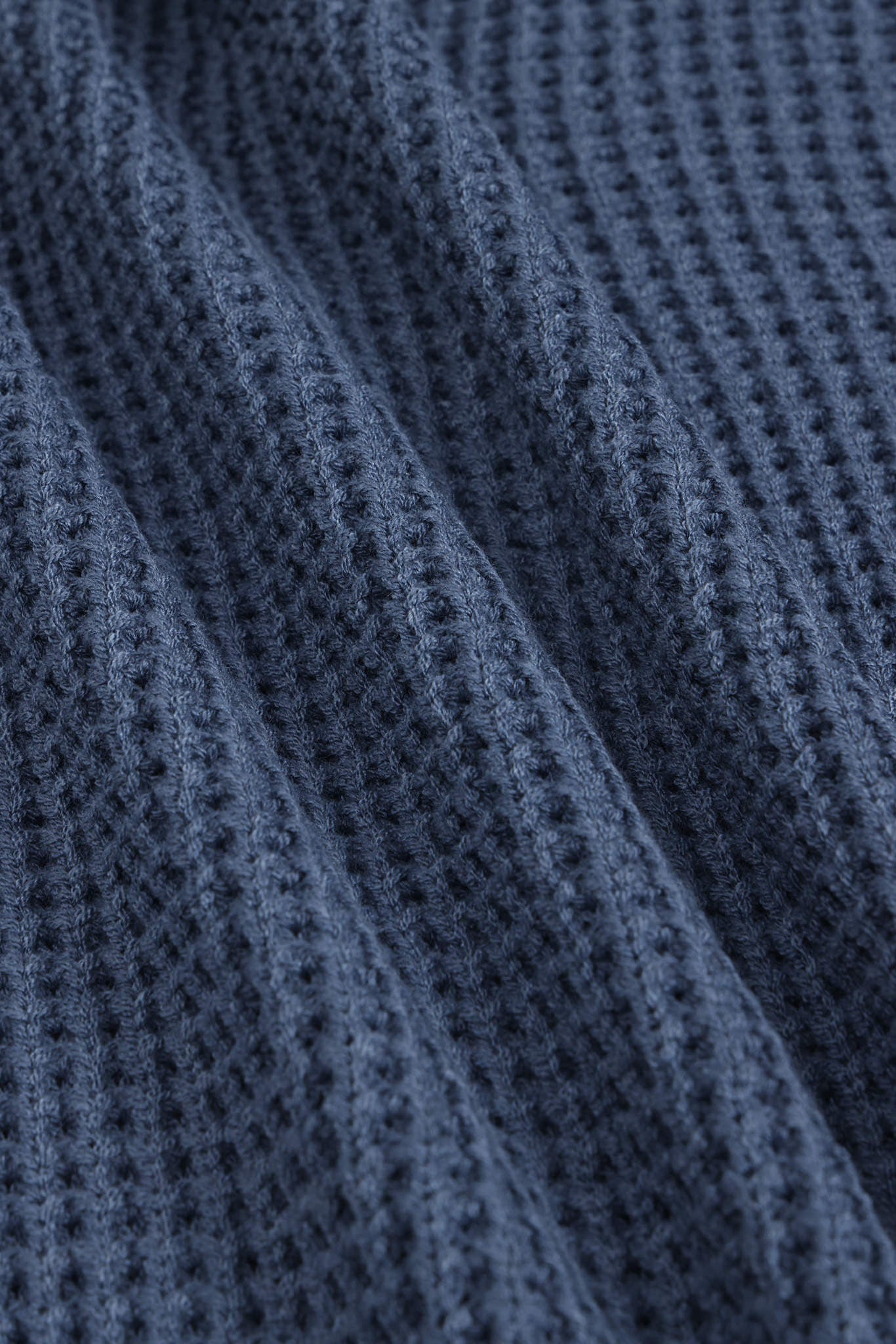 Close-up of a textured navy blue knit fabric with a waffle or open-stitch pattern, shown with soft folds.