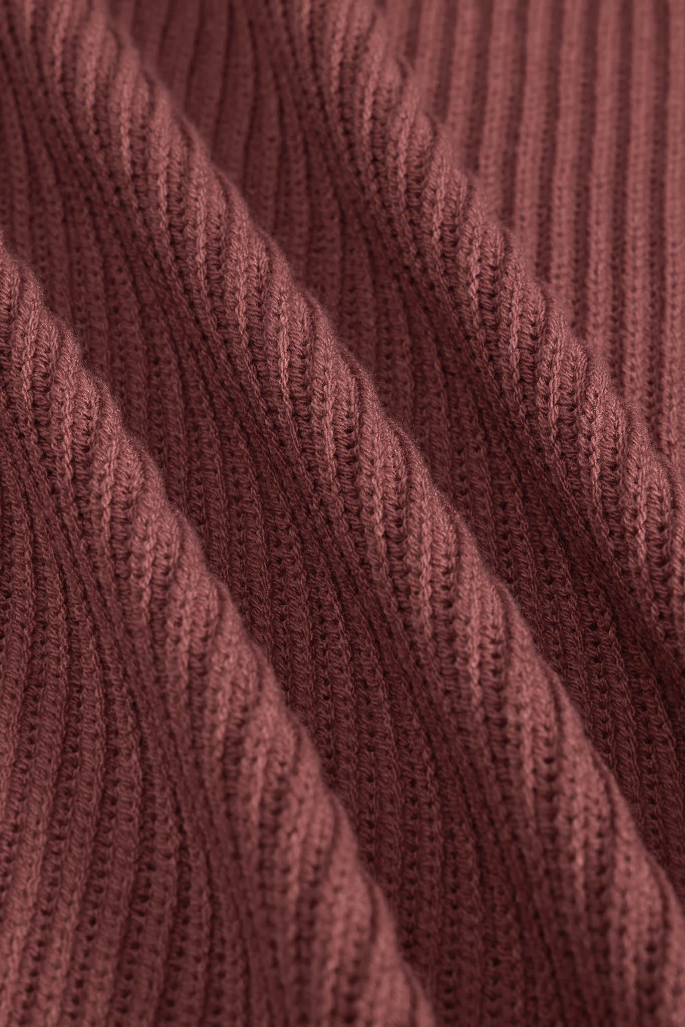Close-up of a ribbed knit fabric in a dusty rose or mauve-brown color, showing the detailed texture and folds of the yarn.