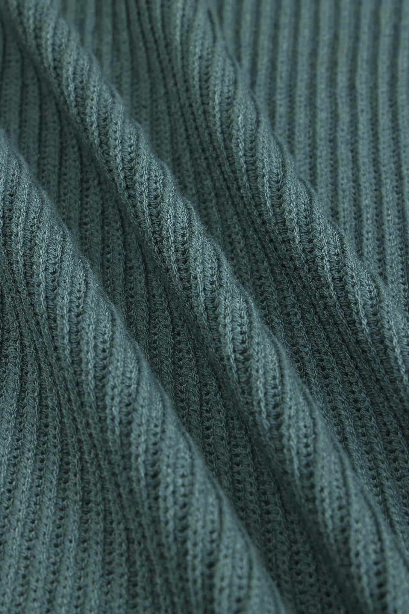 Close-up of a ribbed knit fabric in a muted blue-green color, showing the detailed texture and folds of the material.