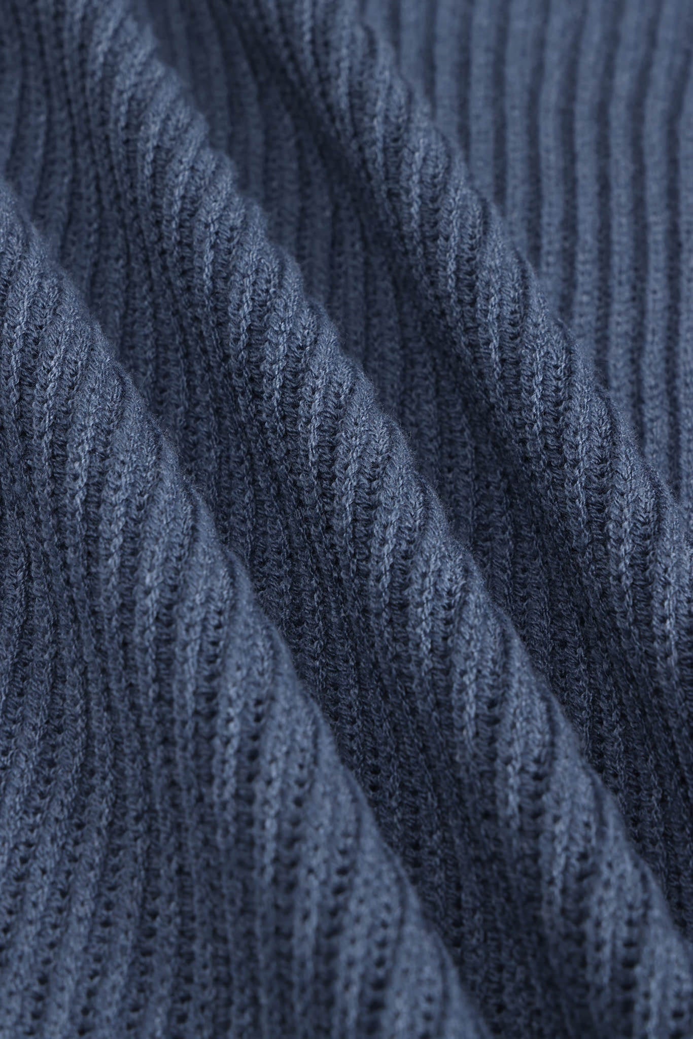 Close-up of a dark blue ribbed knit fabric with diagonal folds showing the detailed knit texture.