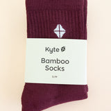 Adult Crew Socks in Burgundy shown in its packaging laying on a light neutral surface