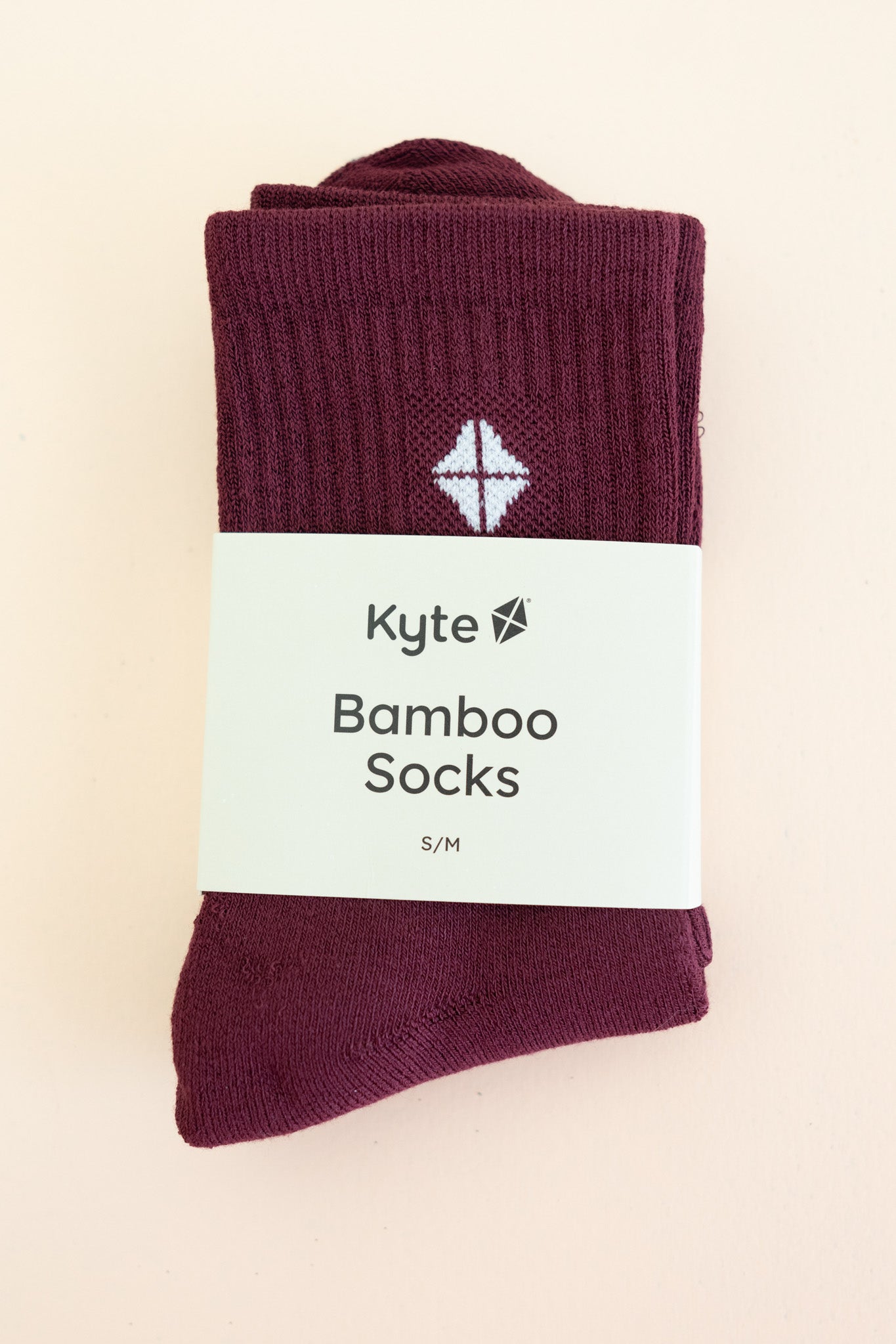 Adult Crew Socks in Burgundy shown in its packaging laying on a light neutral surface