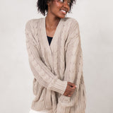Model holding her arms across her front while wearing the Kyte Chunky Knit Cable Cardigan in Almond