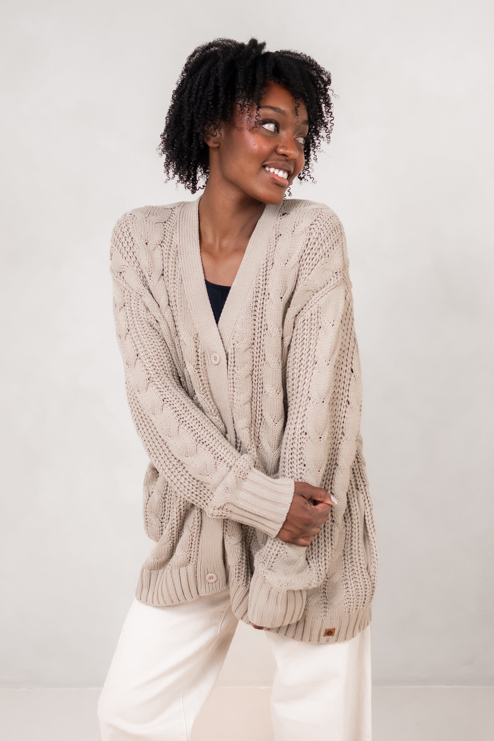 Model holding her arms across her front while wearing the Kyte Chunky Knit Cable Cardigan in Almond