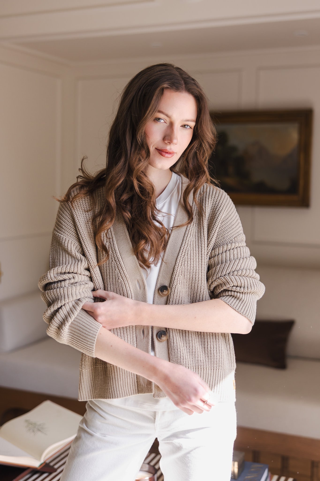Woman soft smiling pulling up her sleeve wearing a cropped cardigan in almond
