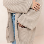 Person wearing a tan knitted cardigan over a white shirt and blue jeans.