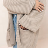 Person wearing a tan knitted cardigan over a white shirt and blue jeans.