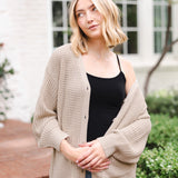 Modal standing outdoors wearing Chunky Knit Women's Waffle Cardigan in Almond over midnight camisole and blue jeans