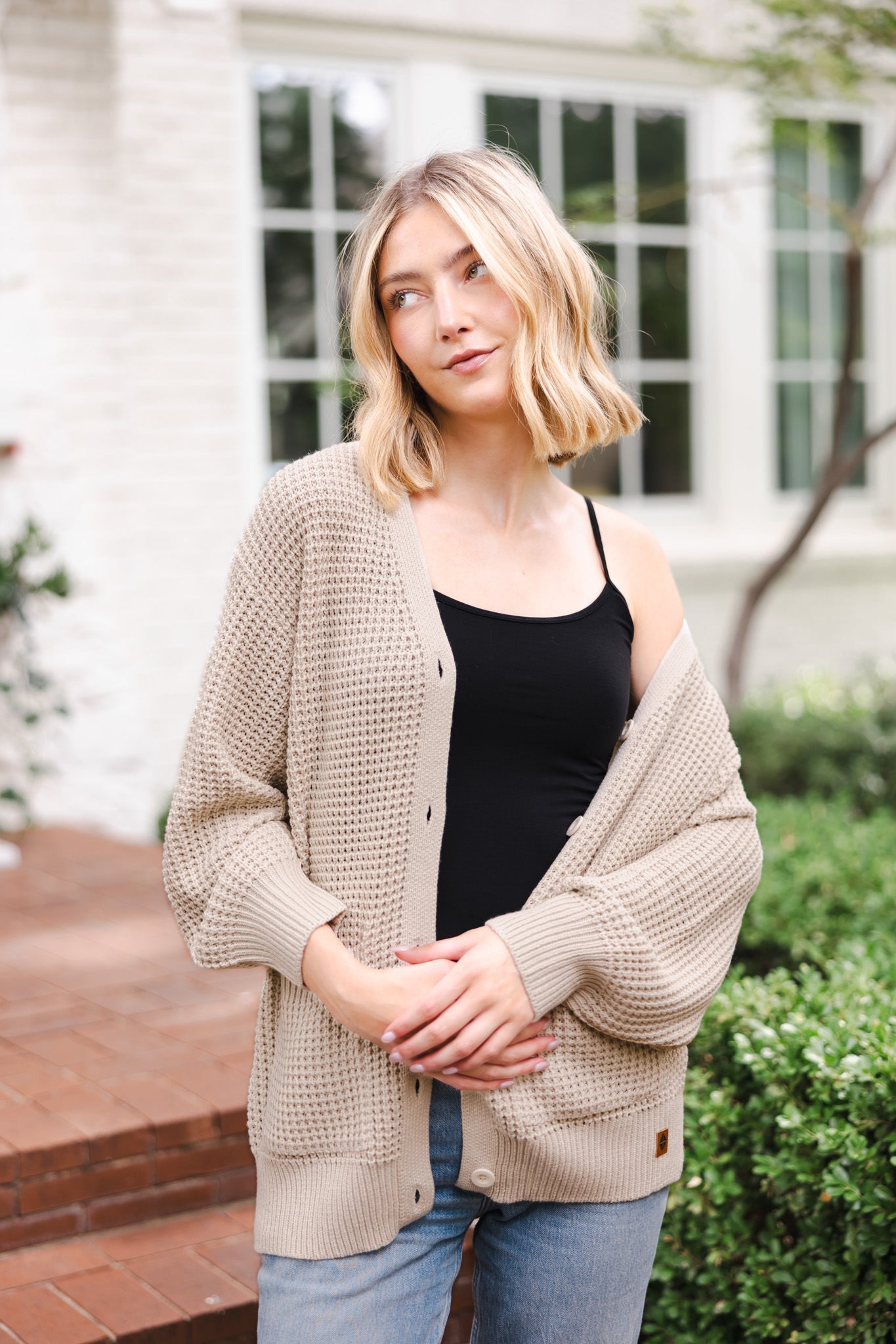 Modal standing outdoors wearing Chunky Knit Women's Waffle Cardigan in Almond over midnight camisole and blue jeans