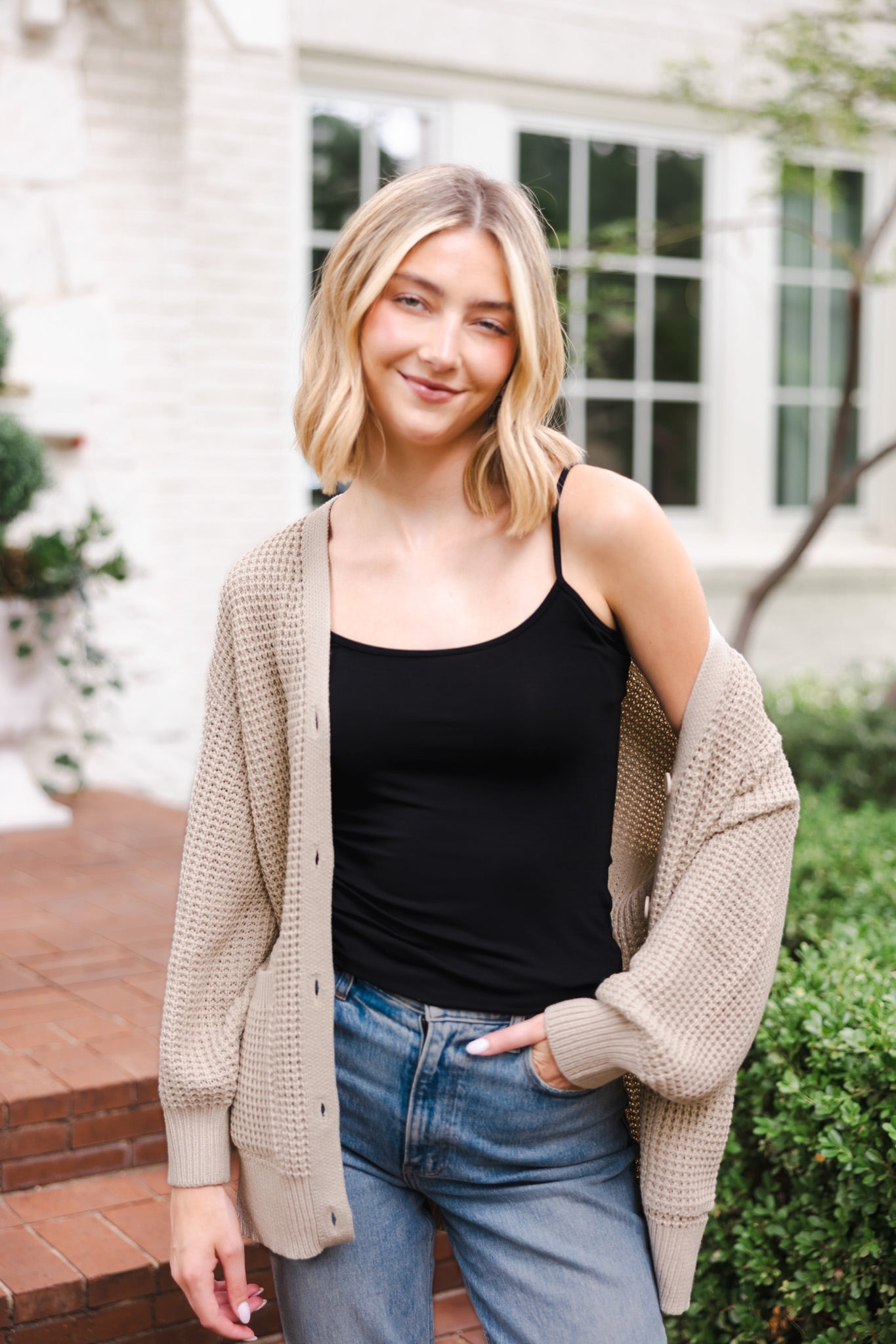 Modal posing outdoors wearing Chunky Knit Women's Waffle Cardigan in Almond over midnight camisole and blue jeans