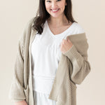 Woman in white outfit modeling Chunky Knit Women's Oversized Cardigan in Almond holidng sweater