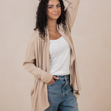 Smiling model standing with one hand in her jeans pocket with the other hand on her head wearing the Women's French Terry Wrap Top in Almond 