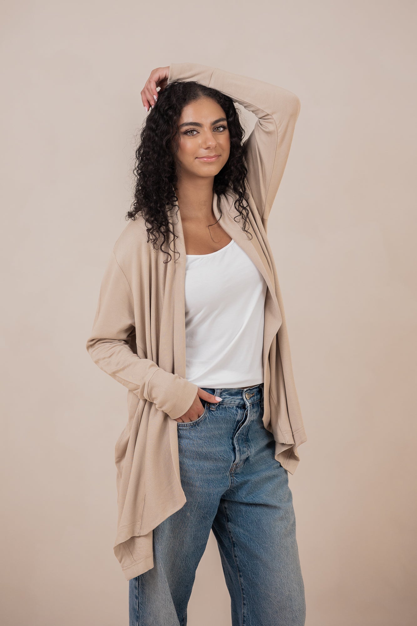 Smiling model standing with one hand in her jeans pocket with the other hand on her head wearing the Women's French Terry Wrap Top in Almond 