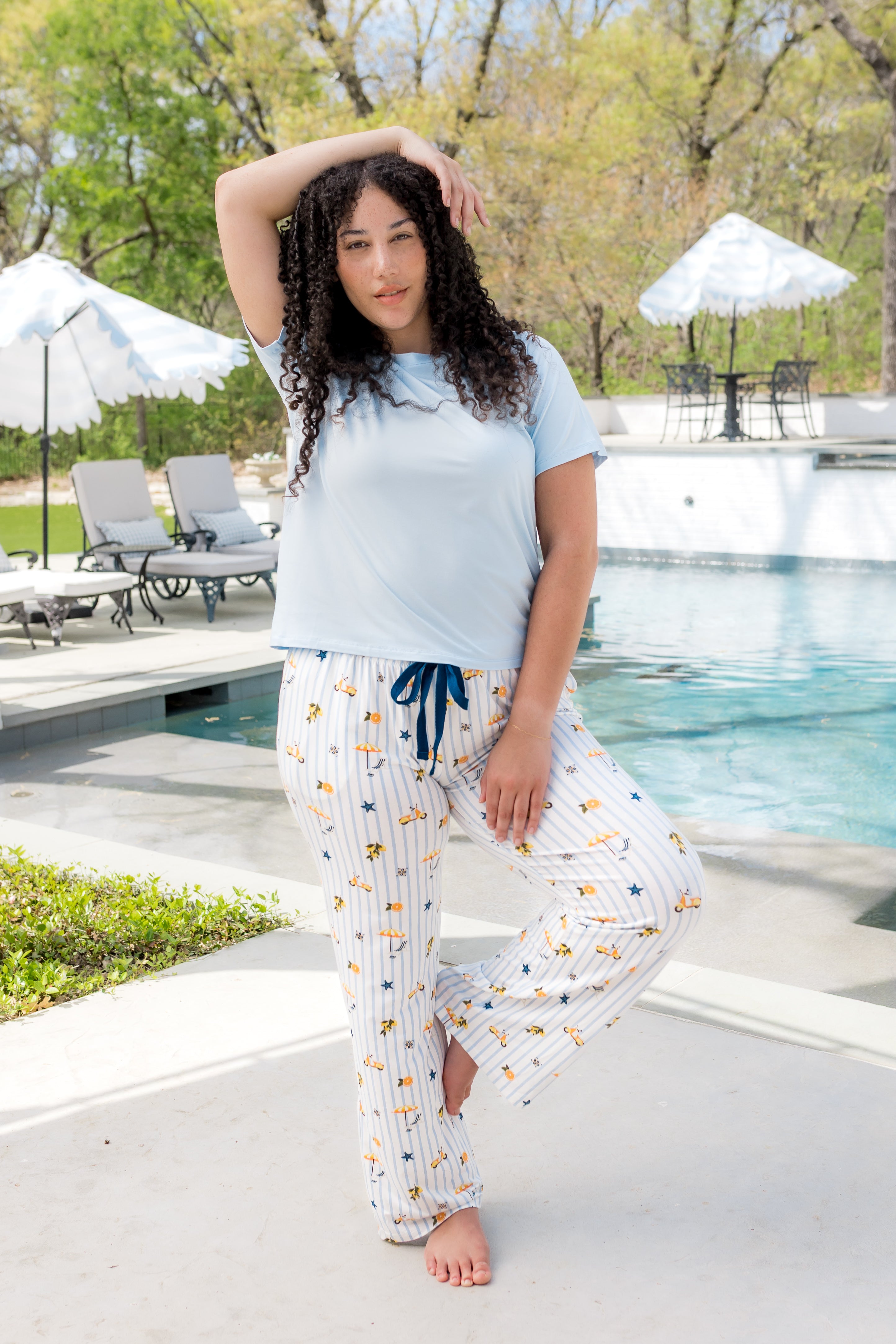 Woman posing outside of a pool with one hand over head while modeling the Women's Lounge Pants in Amalfi Coast paired with a tee in Breeze 