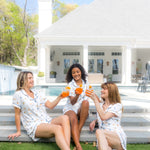 3 Models cheering with orange drinks while wearing matching Women's Short Sleeve Pajama Set in Amalfi Coast on steps 