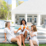 3 Models cheering with orange drinks while wearing matching Women's Short Sleeve Pajama Set in Amalfi Coast on steps 