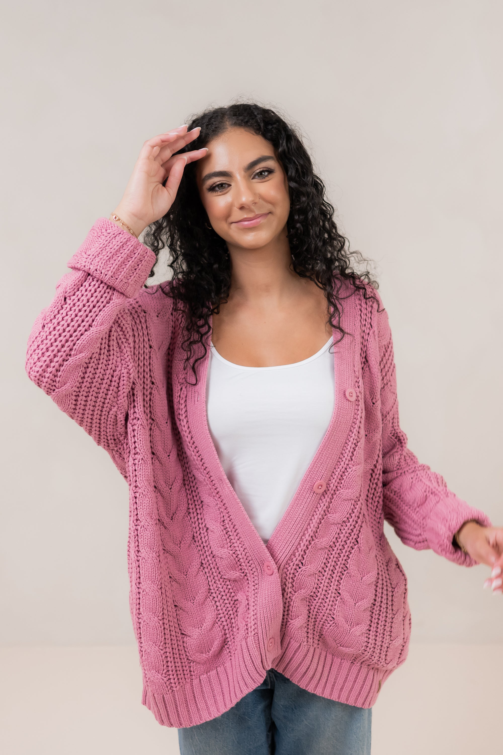 Model with hand in her hair while wearing the  Kyte Cable Knite Cardigan in Apple Blossom paired with jeans