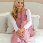 Model sitting on an all white bed while wearing the Adult Sleep Bag Walker in Apple Blossom with a cloud top underneath it 