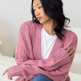 Woman wearing a pink knitted cardigan sitting on a white surface.
