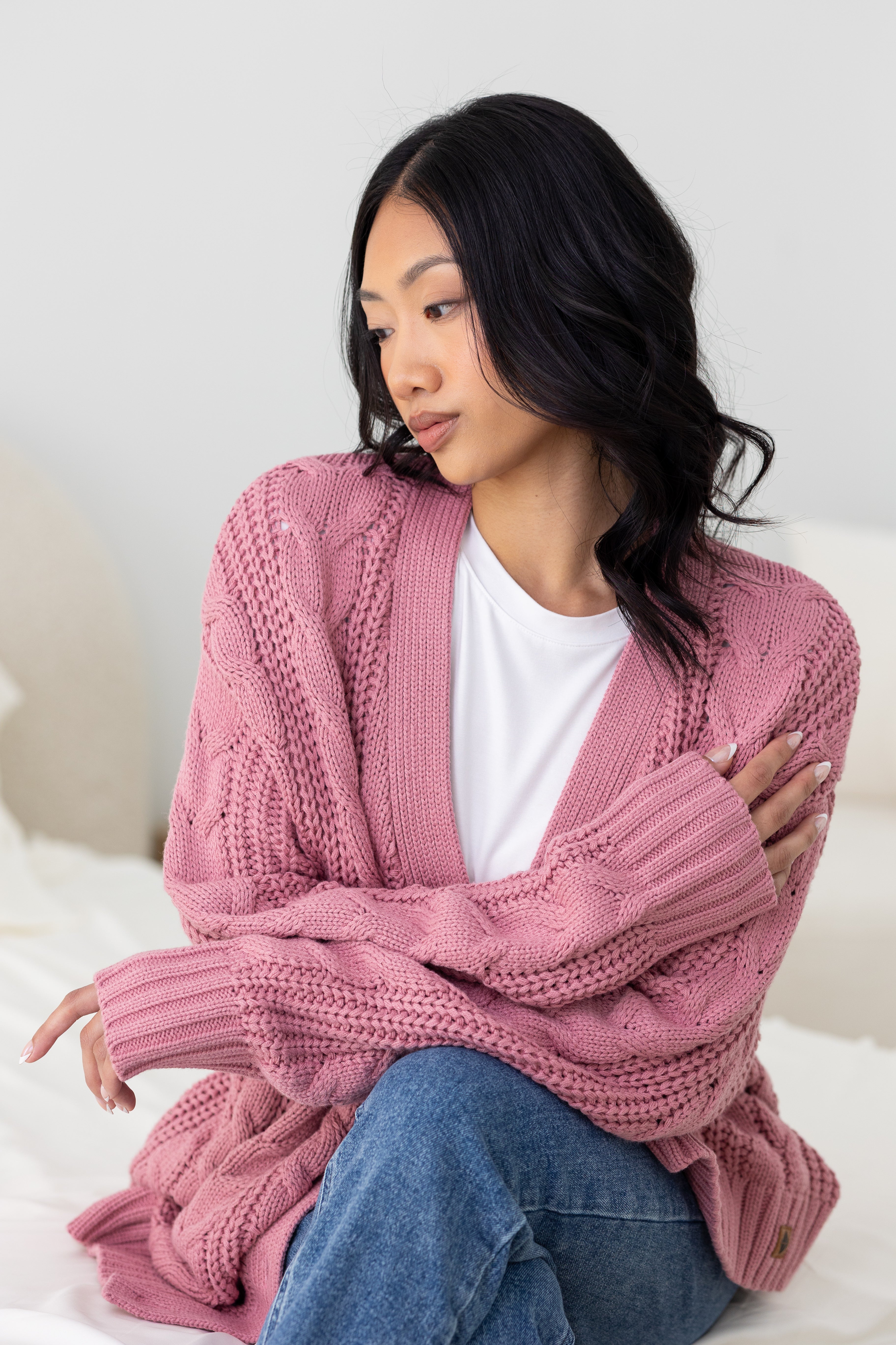 Woman wearing a pink knitted cardigan sitting on a white surface.