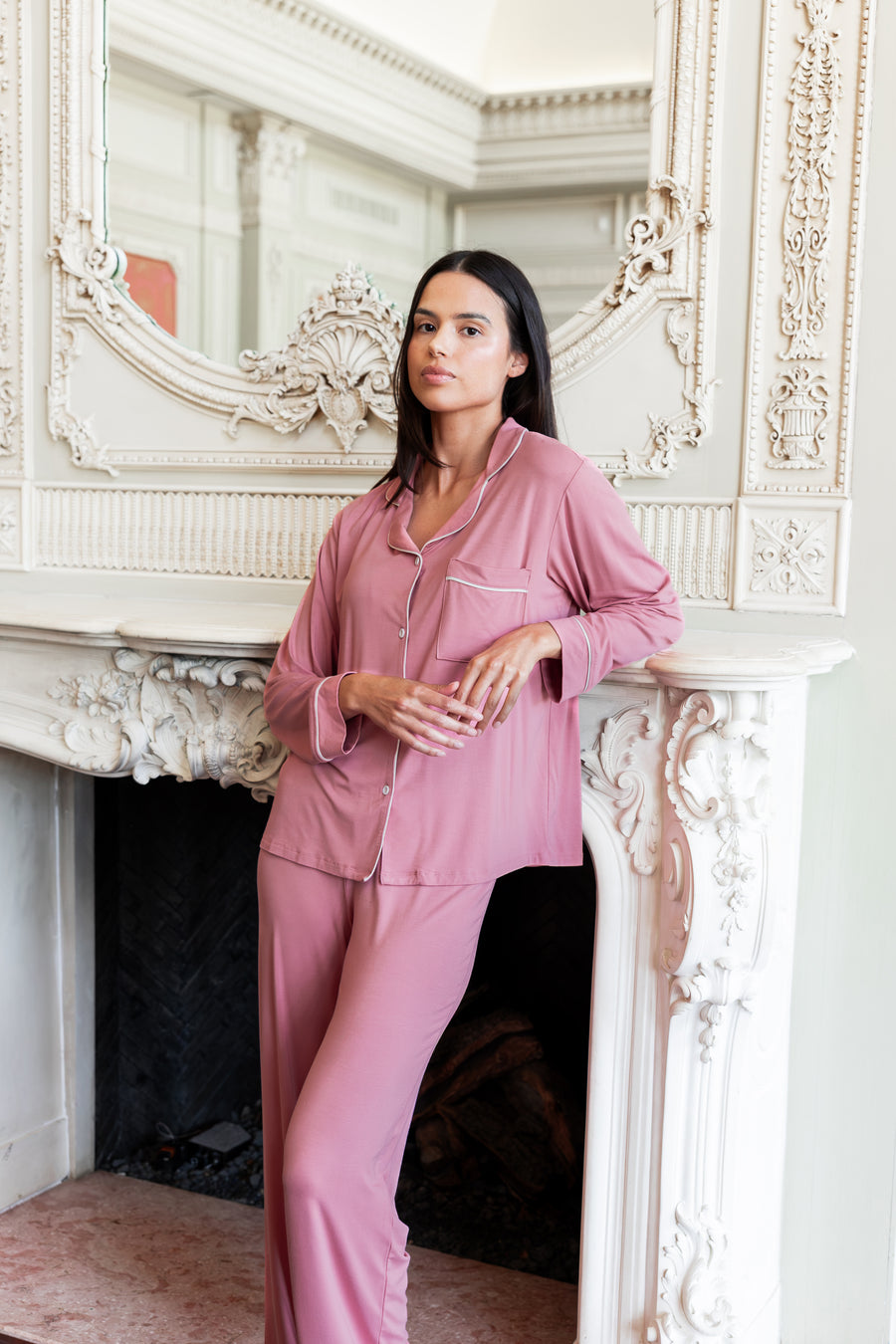 Woman leaning on a fireplace with her arm propped up wearing a long sleeve pajama set in apple blossom.