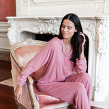 A woman wearing a dusty pink pajama set sits on an ornate pink velvet armchair in front of a white fireplace mantel.
---1605 1