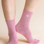 A pair of light pink ribbed ankle socks worn on a person's feet, shown against a solid light beige background.