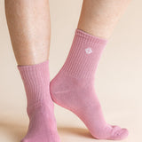 A pair of light pink ribbed ankle socks worn on a person's feet, shown against a solid light beige background.